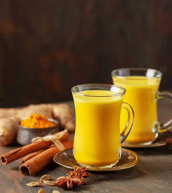 two mugs filled with orange juice next to cinnamon sticks and cloves on a table