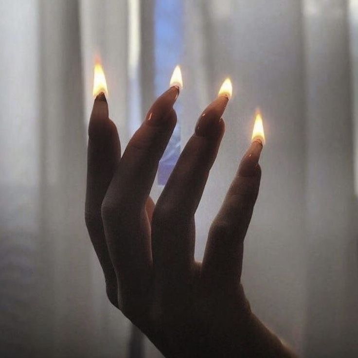 a person holding out their hand with two lit candles in front of them, on a window sill