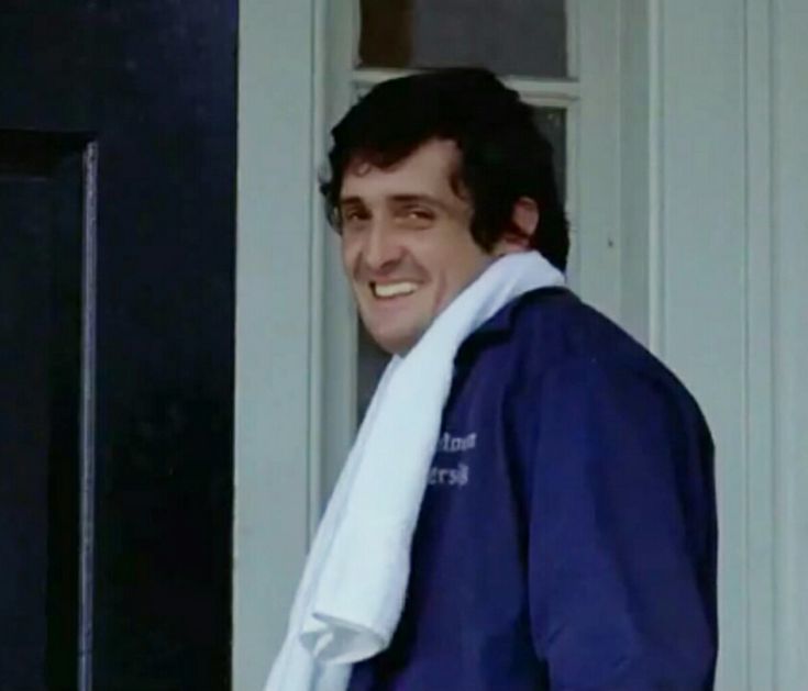 a man with a towel wrapped around his neck standing in front of a door and smiling