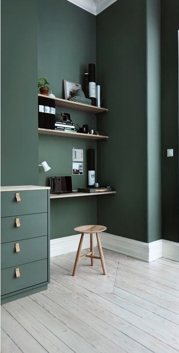 an office with green walls and wooden flooring in the corner, there is a small stool on one side of the desk