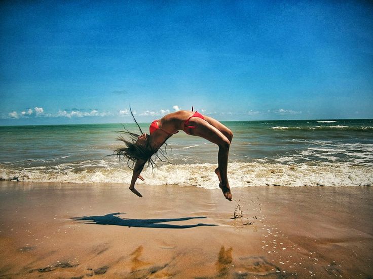 a woman doing a handstand on the beach with her feet in the air