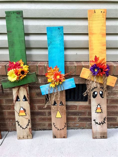 three scarecrows made out of wood sticks with flowers in them sitting next to a brick wall