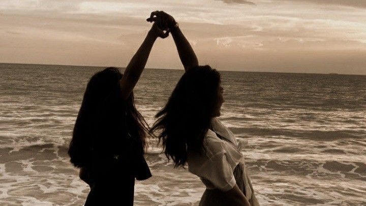 two women standing on the beach with their arms in the air