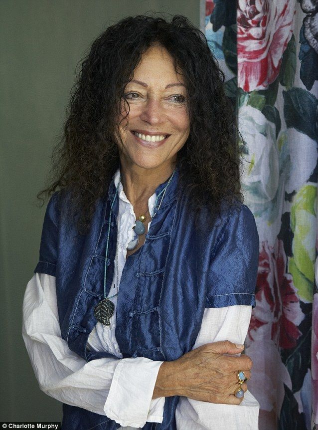 a woman standing in front of a curtain with her arms crossed and smiling at the camera