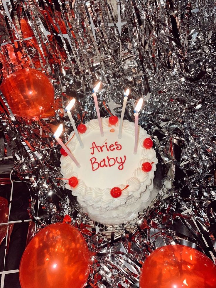 a birthday cake with candles on it surrounded by red balloons