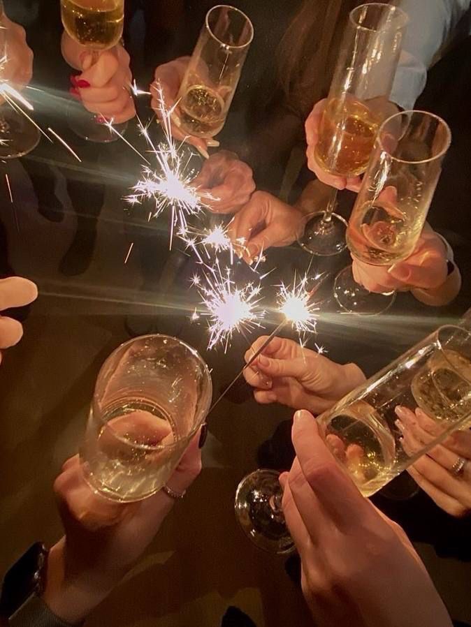 many people holding wine glasses with sparklers in them