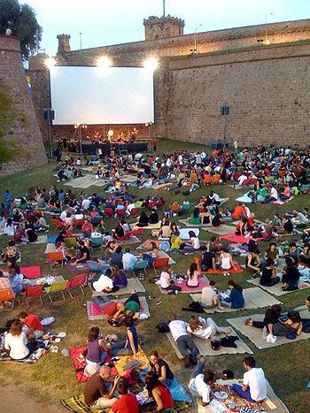 an outdoor movie theater with people sitting on the grass