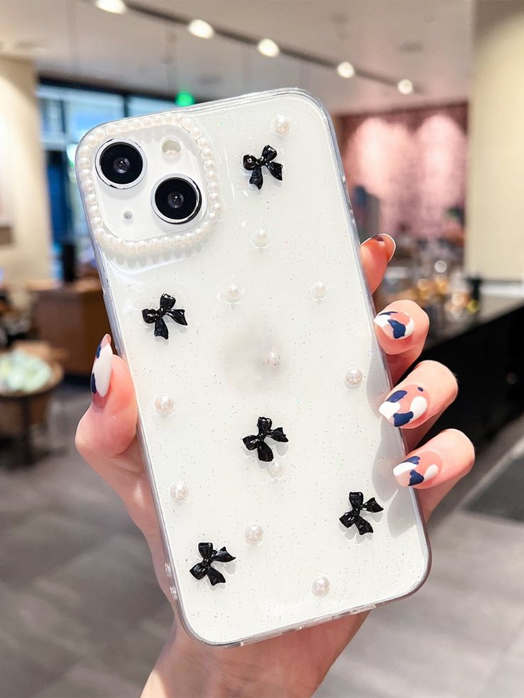 a woman holding up her phone case with pearls and bows on it