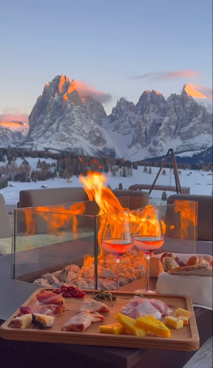 two glasses of wine and cheese on a table with mountains in the background at sunset