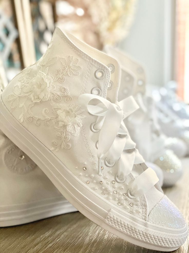 two white shoes with bows on them sitting on top of a wooden table in front of a mirror