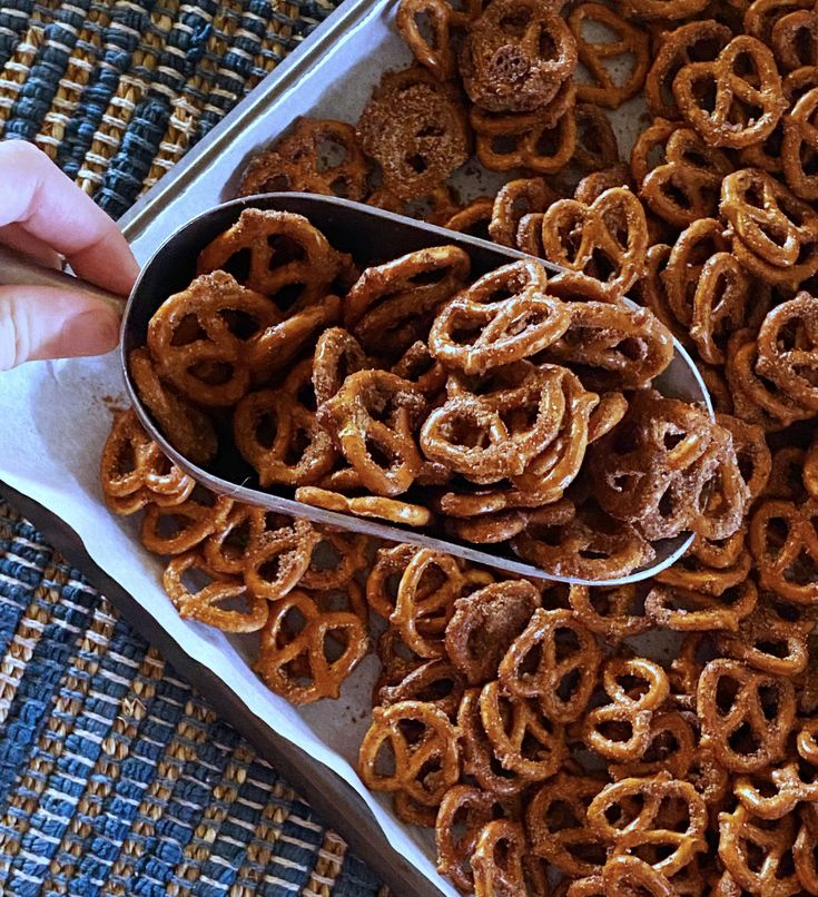 a person holding a spoon full of pretzels in front of a tray filled with them