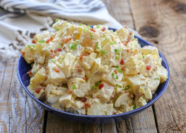 a blue bowl filled with potato salad on top of a wooden table