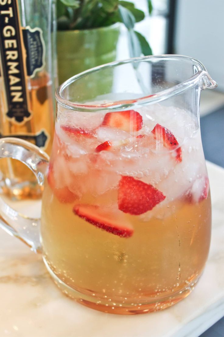 a pitcher filled with ice and strawberries on top of a table next to a bottle