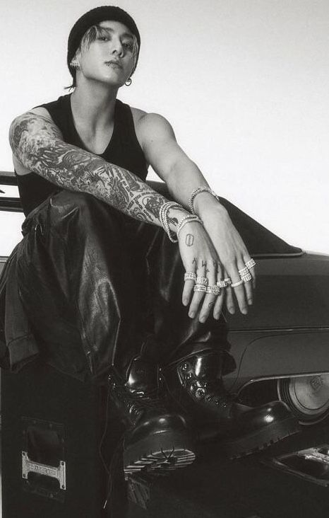 a black and white photo of a man sitting on top of a car with tattoos