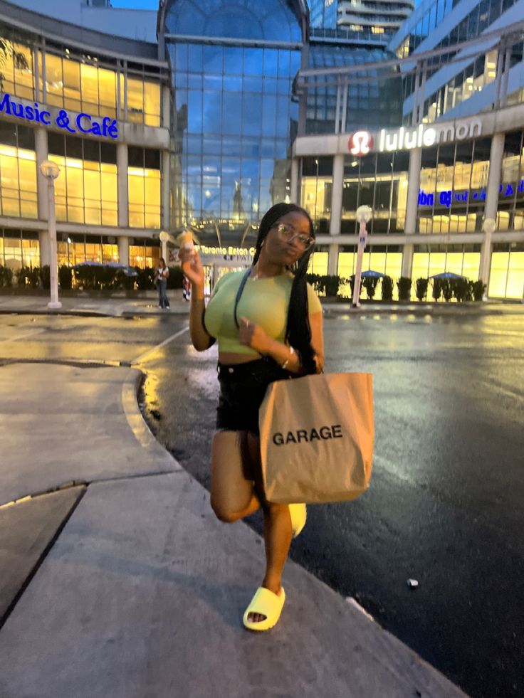 a woman in yellow shirt and black shorts holding a brown bag walking down the street