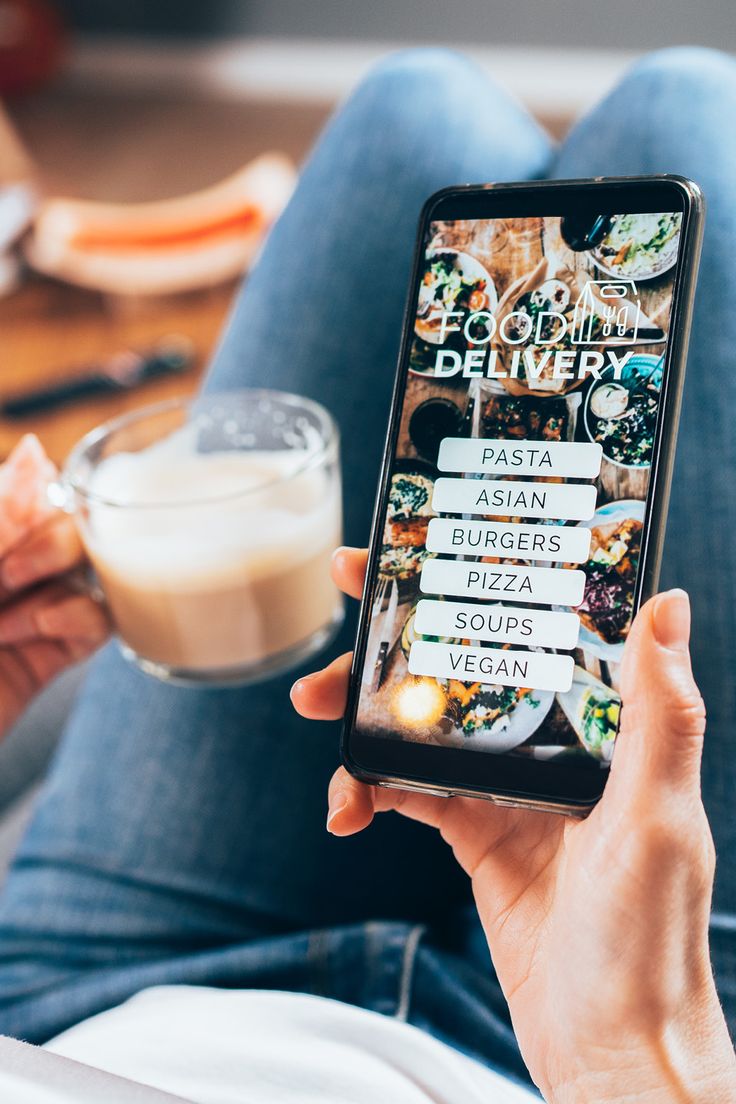 a person sitting on the floor holding up a cell phone with food and drinks in front of them