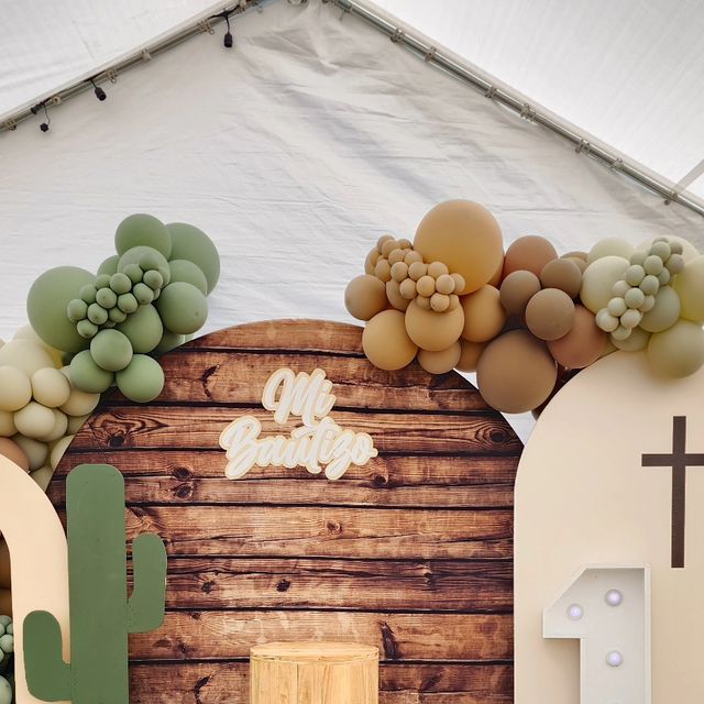 a wooden wall decorated with balloons and greenery in front of a white canvas tent