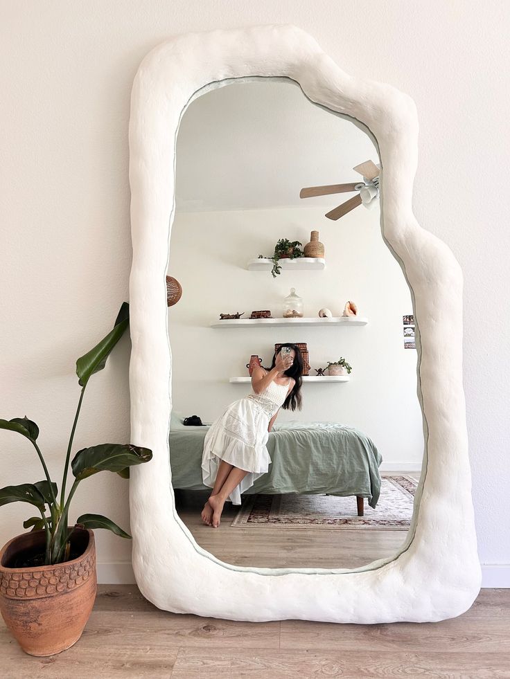 a woman taking a selfie in front of a large white mirror on the floor