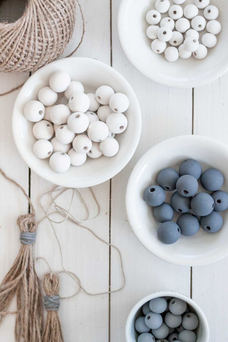 three bowls filled with beads and twine on top of a white wooden table next to yarn