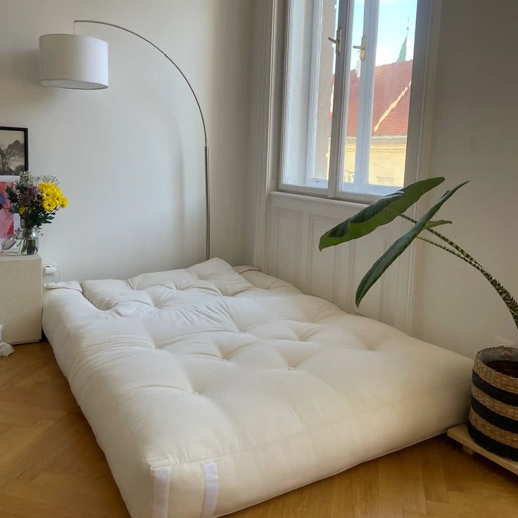 a white futon mattress sitting in front of a window next to a potted plant