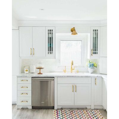 a kitchen with white cabinets and stainless steel dishwasher in the center, gold accents