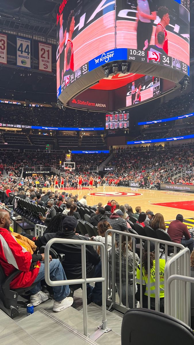 people sitting in chairs watching a basketball game on the big screen at an indoor arena