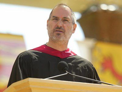 a man standing at a podium in front of a microphone and wearing a graduation gown