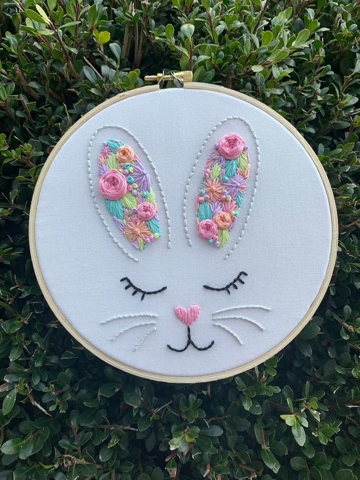 an embroidered bunny rabbit face with flowers on it's ears is shown in front of some bushes