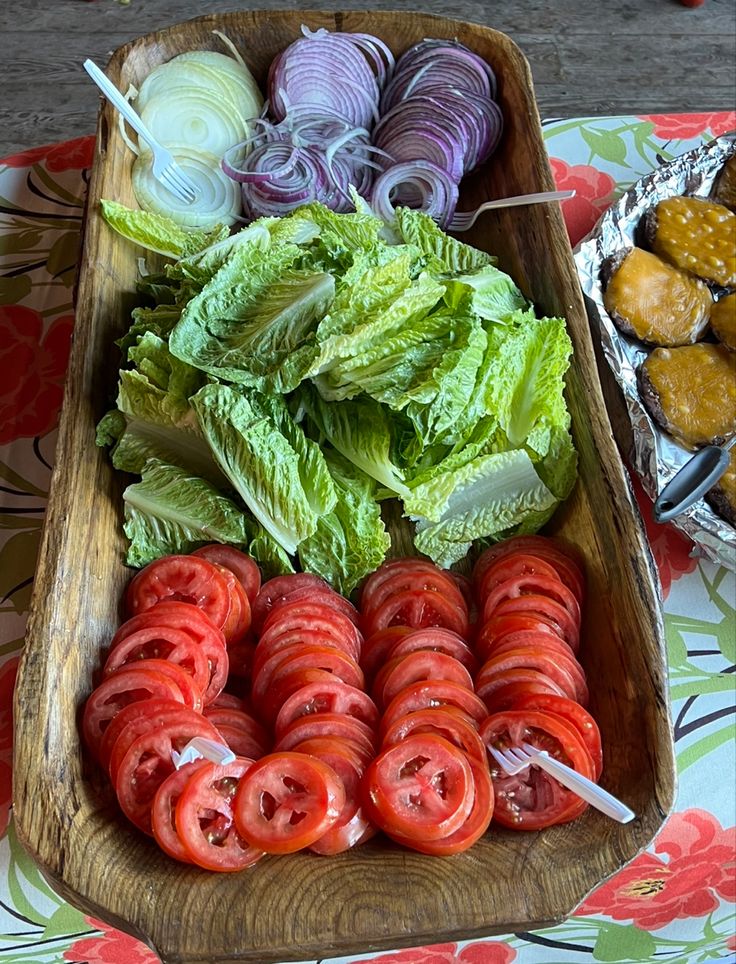 lettuce, tomatoes, and other vegetables are on display in a wooden tray