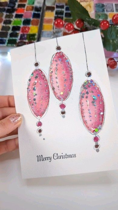 a card with three pink christmas ornaments hanging from it