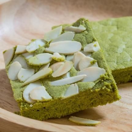 two pieces of green cake on a wooden plate with almonds and pistachio