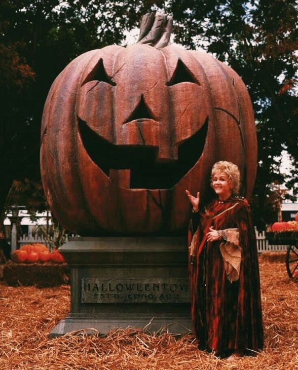 a woman standing next to a carved pumpkin