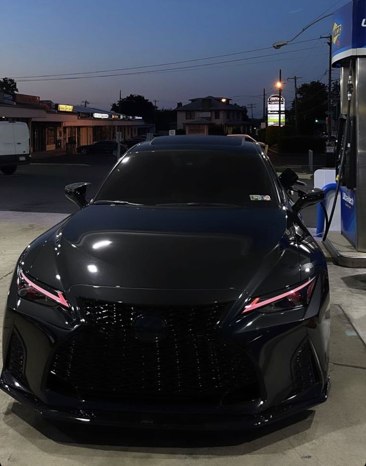 a black sports car is parked at a gas station with its hood up and lights on