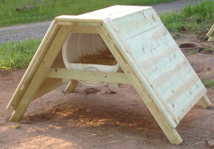 a dog house made out of pallets on the ground with grass and dirt around it