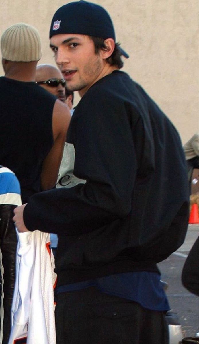 a man in black jacket and hat standing next to a skateboard with other people behind him