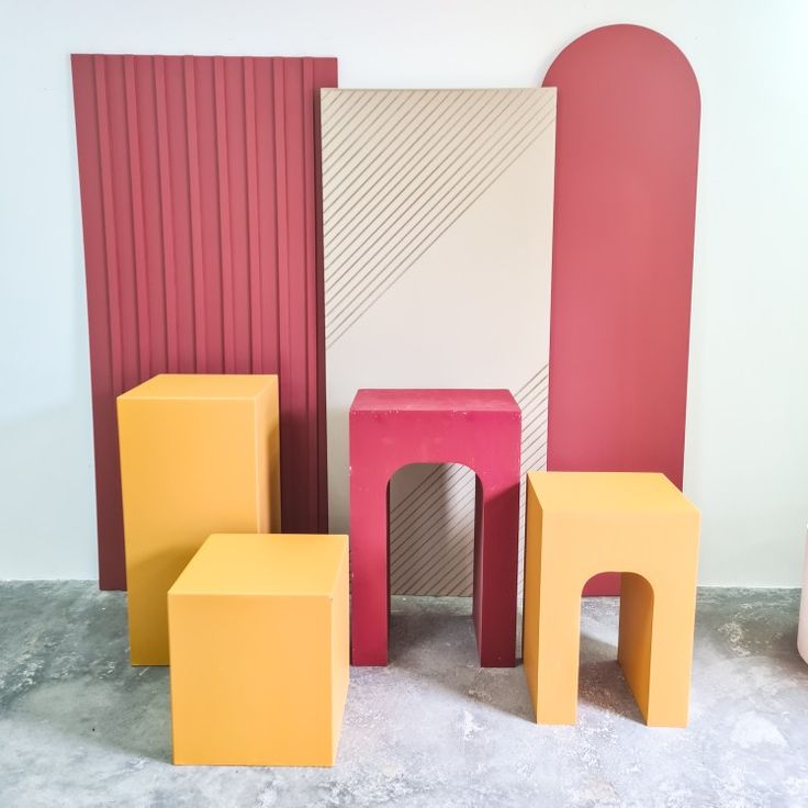 several different colored stools and tables in front of a wall with red, pink, yellow, and white panels