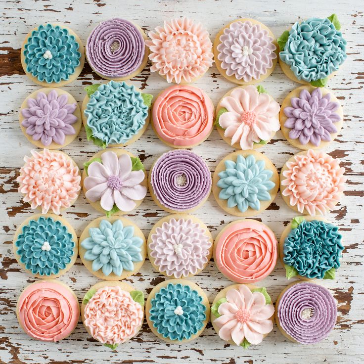 decorated cupcakes arranged in the shape of flowers on a white wooden background with pink, blue and green icing