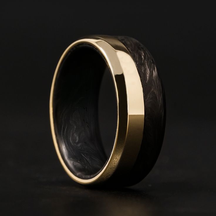 a black and gold wedding ring with an intricate design on the inside, sitting on a dark surface