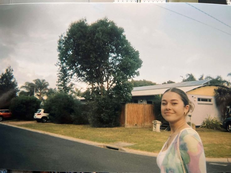 a woman standing in front of a house next to a street with cars parked on it