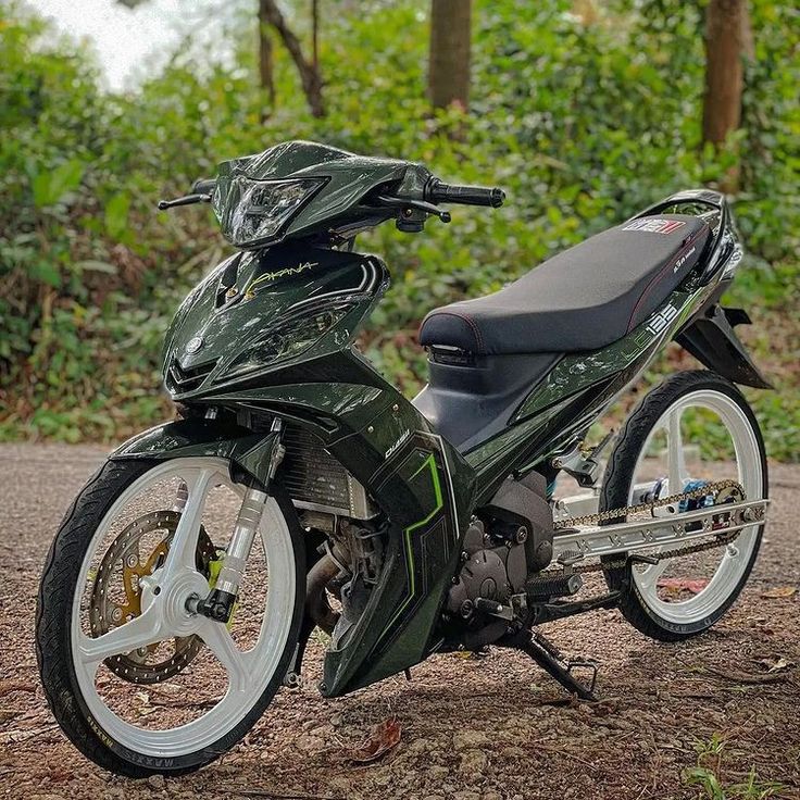 a green motorcycle parked on the side of a road in front of trees and bushes