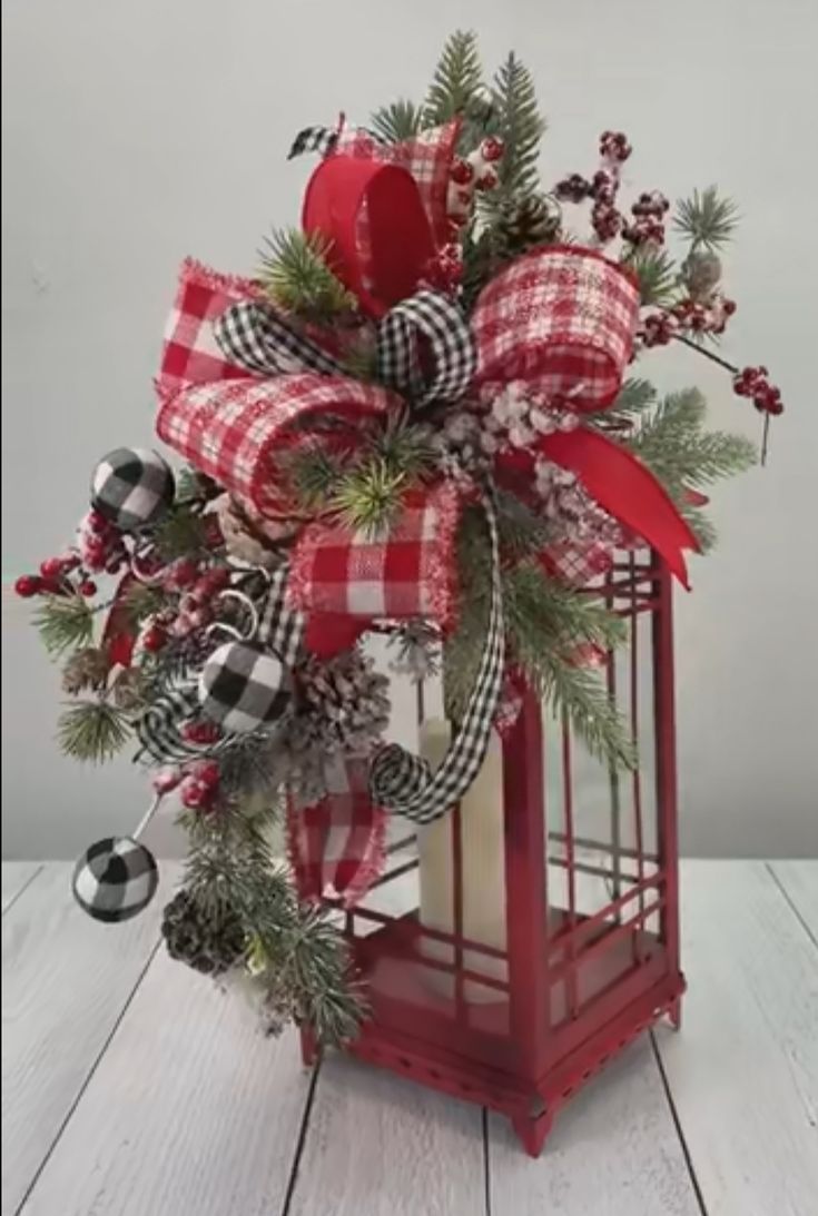 a red lantern decorated with pine cones, berries and plaid ribbon is sitting on a wooden table