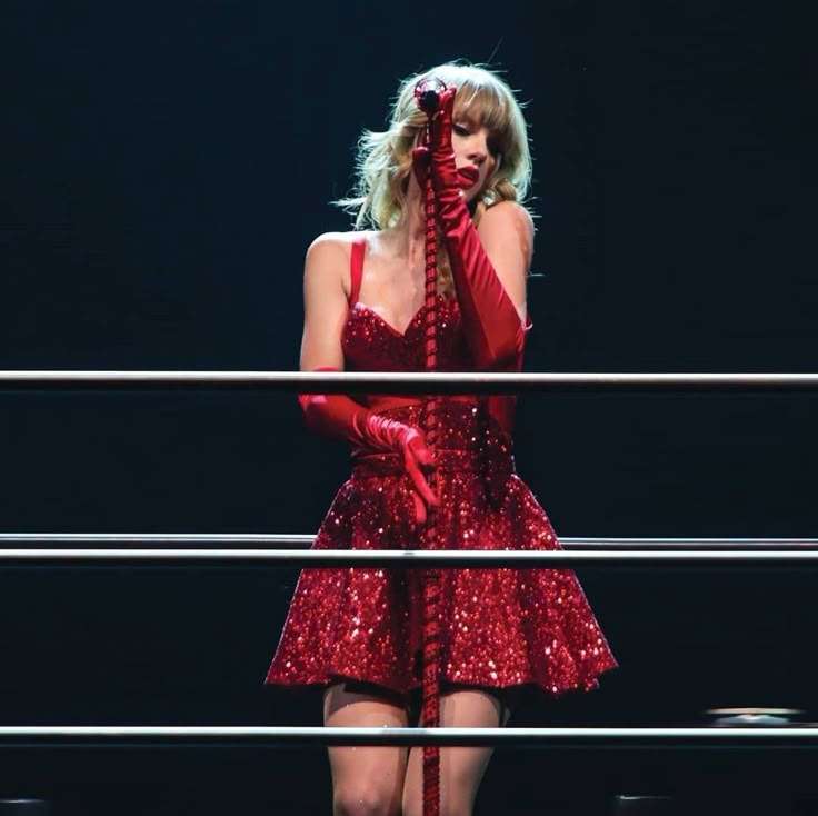 a woman in a red dress on stage with her hands over her face and microphone to her mouth