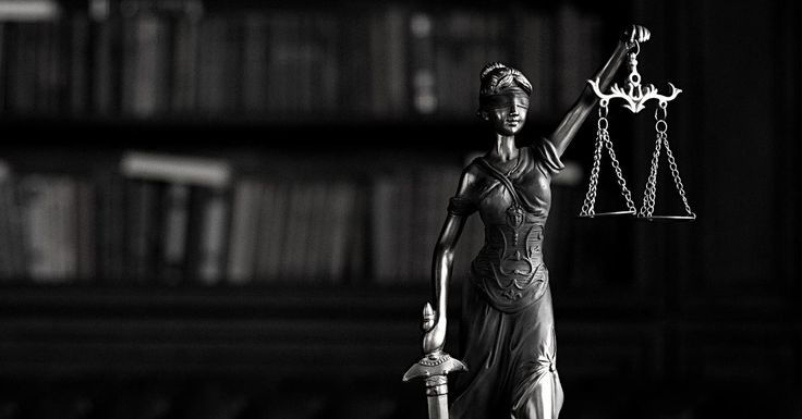 a statue of lady justice holding a scale in front of a bookcase with books on it