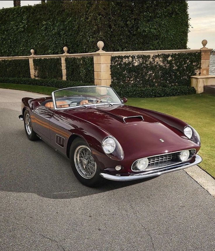 a red sports car parked on the side of a road next to some bushes and trees