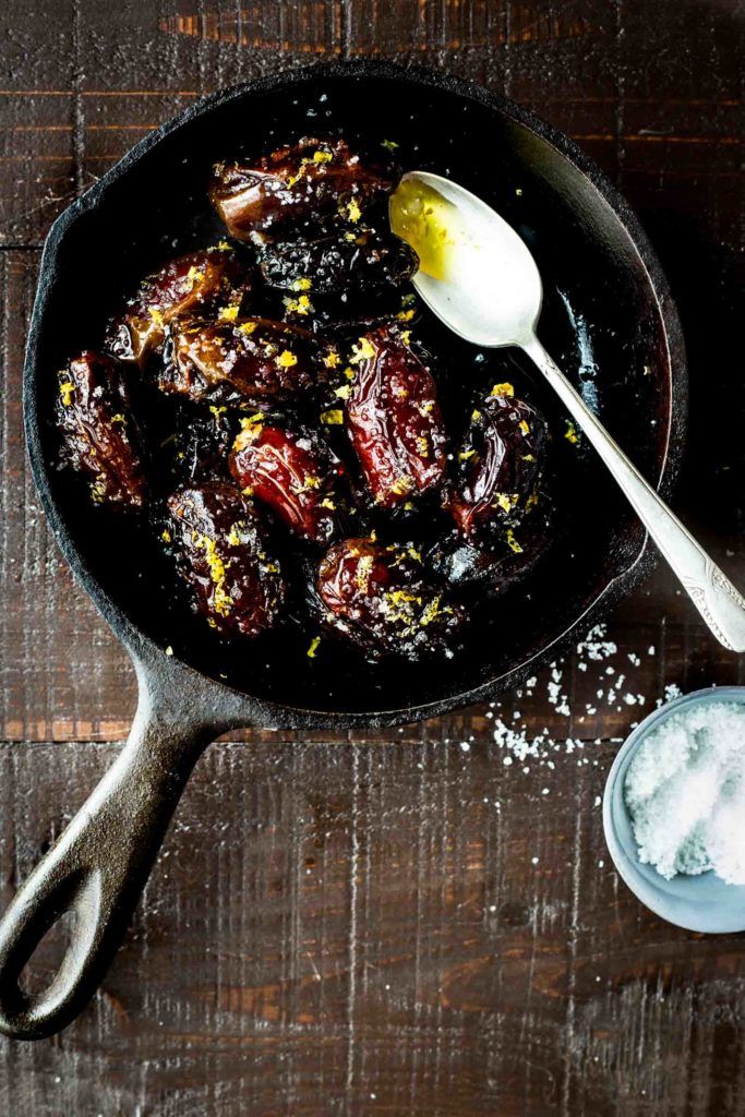 an iron skillet filled with food on top of a wooden table next to two spoons