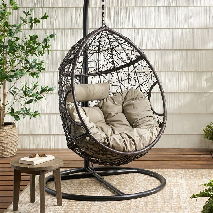 a hanging egg chair with cushions on the outside patio, next to a potted plant