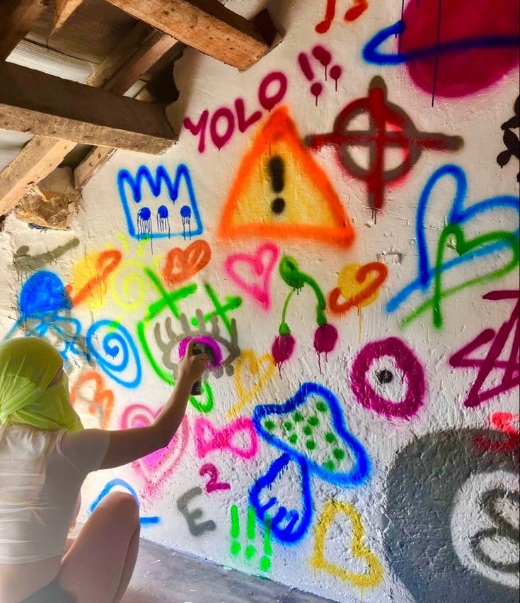 a person kneeling down in front of a wall with graffiti on it's walls