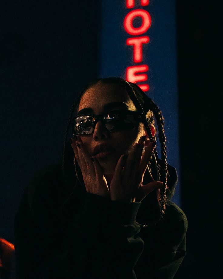 a woman with glasses is holding her hand to her face in front of a neon sign