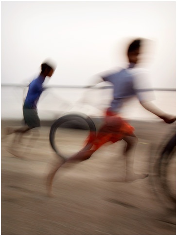 blurry photograph of two people riding bikes on the beach with one person running behind them