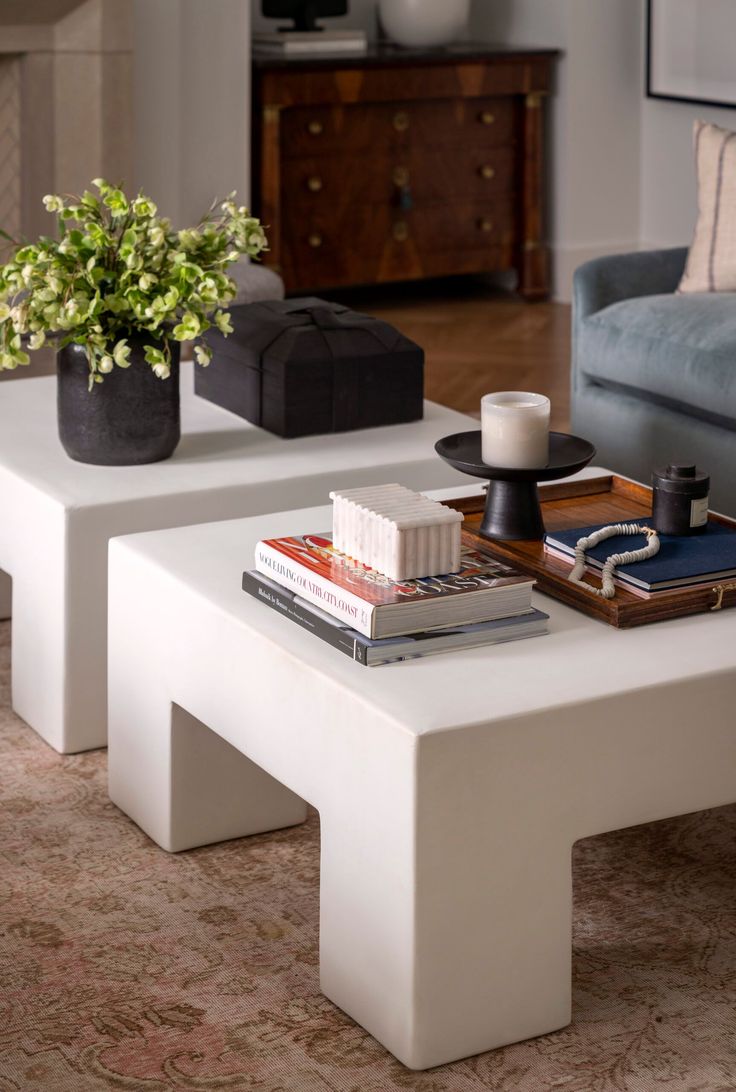 two white tables with books on them in a living room area next to a couch and coffee table